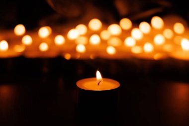 Odakta bir mum parlıyor, arka planda paskalya bağlılığını temsil eden bulanık bokeh ışıklarıyla çevrili.