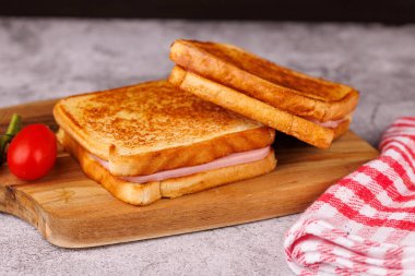 Ağız sulandıran peynir ve jambonlu sandviçler, taze domateslerle süslenmiş, parlak beton bir masada sergileniyor.