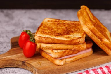 Lezzetli bir peynir ve jambonlu sandviç. Taze domateslerle birlikte. Siyah beton bir yüzey üzerinde güzelce sunuluyor.