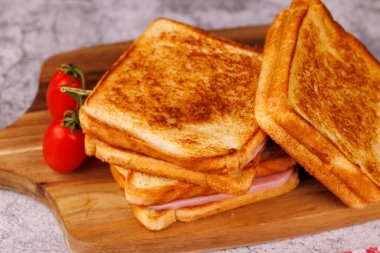 Lezzetli bir peynir ve jambonlu sandviç çeşidi, yanında olgun domatesler, zarif bir şekilde siyah beton bir masa üzerine dizilmiş.