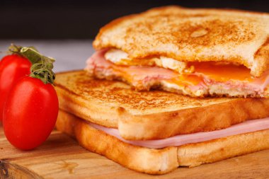 Çeri domatesli peynirli ve jambonlu sandviçlerin harika bir kombinasyonu. Koyu bir yüzeyde kırmızı kareli peçeteyle sunuluyor.