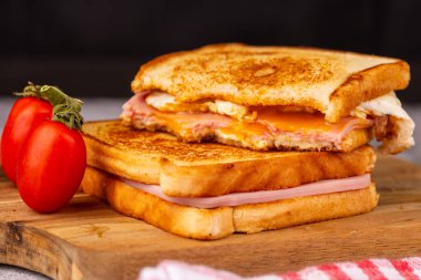 Kırmızı kareli peçeteyle siyah arka planda tamamlanmış vişneli domatesli peynirli ve jambonlu sandviçlerin büyüleyici gösterisi.