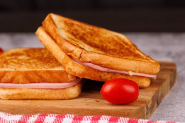 Lezzetli bir peynir ve jambonlu sandviç seçimi, kiraz domateslerinin yanında, kırmızı kareli peçeteyle ustalıkla düzenlenmiş.