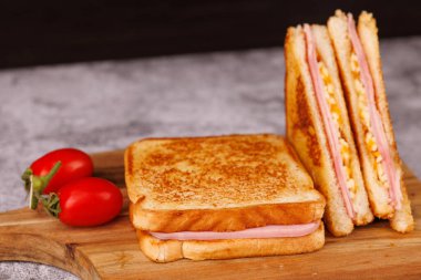 Ağız sulandıran jambonlu ve peynirli sandviçler, ikiye bölünmüş ve zarif bir beton masada siyah bir arka plana karşı sunulmuş.