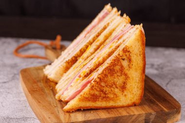 Lezzetli bir jambonlu ve peynirli sandviç seçimi. Beton bir masada, çarpıcı bir siyah arkaplana karşı ustalıkla ikiye bölünmüş.