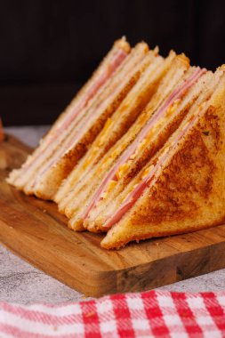 Cazip bir jambonlu ve peynirli sandviç seçimi. İkiye bölünmüş ve zarif bir şekilde beton bir masada koyu siyah bir arka plana karşı dizilmiş.