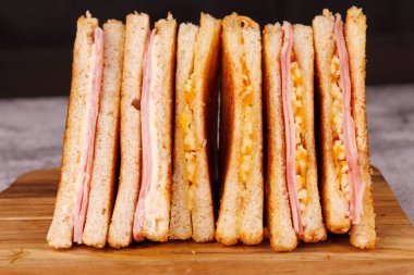 İkiye bölünmüş jambonlu ve peynirli sandviçlerden oluşan tatmin edici bir seçim. Koyu beton bir masada zarif bir şekilde sunuluyor.