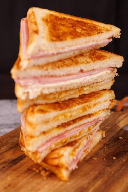 İkiye bölünmüş jambonlu ve peynirli sandviçlerden oluşan büyüleyici bir dikey düzenleme, siyah arka planda gri beton bir masada zarif bir şekilde sunuluyor.