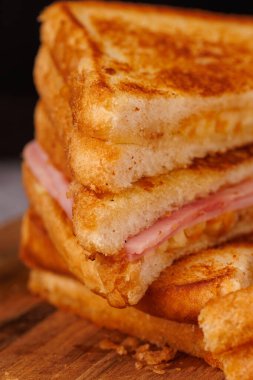 Dikey, zarif bir şekilde gri beton bir masada duran koyu siyah arkaplanlı jambonlu ve peynirli sandviçlerin tatmin edici bir seçimi.
