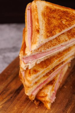 Dikey bir kule oluşturan jambonlu ve peynirli sandviçlerin büyüleyici gösterisi, siyah arkaplanlı gri beton bir masa üzerinde zarif bir şekilde düzenlenmiştir.