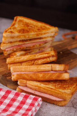 Ağız sulandıran jambonlu ve peynirli sandviçler dikey bir kule oluşturuyor. Gri beton bir masada, siyah bir arka planı var.