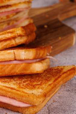 Dikey ve güzel bir şekilde, çarpıcı siyah bir arka planla gri beton bir masada sunulmuş jambonlu ve peynirli sandviçlerden oluşan büyüleyici bir düzenleme.