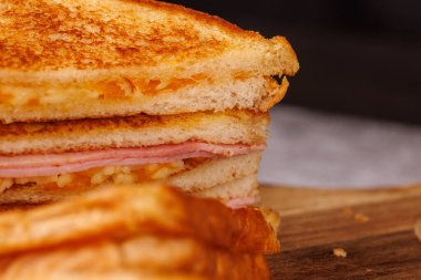 Dikey istiflenmiş, iştah açıcı bir jambonlu ve peynirli sandviç, gri beton bir masada canlı kırmızı vişneli domateslerle eşleştirilmiş.