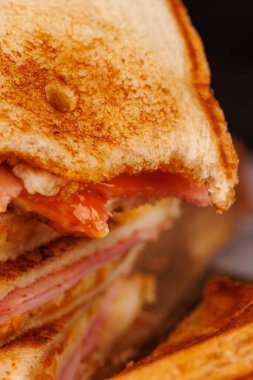 Lezzetli yarısı yenmiş bir yumurta, jambon ve peynir sandviçi dikey bir kulenin tepesinde duruyor. Yanında da koyu kırmızı kiraz domatesleri var.