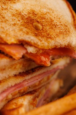 Lezzetli yarısı yenmiş yumurta, jambon ve peynirli sandviç dikey bir kulede sergilenir, gri bir masada taze vişneli domateslerle eşleştirilir.