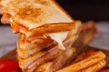 Ağız sulandıran yarısı yenmiş yumurta, jambon ve peynir sandviçi, üzerinde koyu ahşap bir yüzey üzerinde taze kiraz domatesleri ile dikey olarak istiflenir.