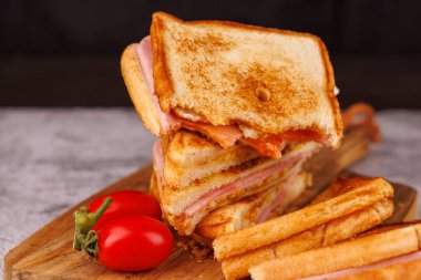 Büyüleyici yarısı yenmiş bir yumurta, jambon ve peynirli sandviç dikey bir kulenin tepesinde duruyor. Siyah tahtada güzel bir şekilde kırmızı kiraz domatesleri sunuluyor.