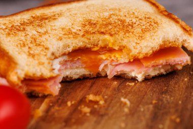 Lezzetli bir yarısı yenmiş yumurta, jambon ve peynirli sandviç dikey bir kulede duruyor. Gri bir masada kırmızı vişneli domateslerle zarif bir şekilde eşleştirilmiş.