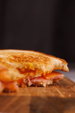 Lezzetli bir yarısı yenmiş yumurta, jambon ve peynirli sandviç dikey bir kulede duruyor. Gri bir masada kırmızı vişneli domateslerle zarif bir şekilde eşleştirilmiş.