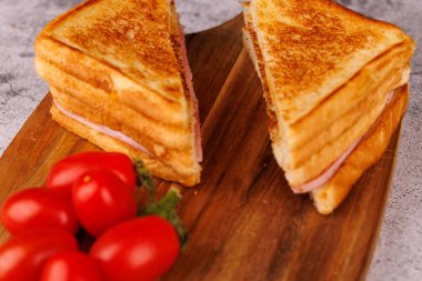 İkiye bölünmüş nefis bir jambonlu ve peynirli sandviç koyu ahşap kesme tahtasındaki taze kiraz domateslerinin yanında oturur.