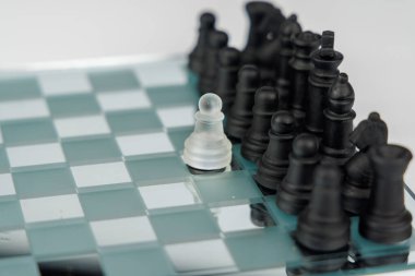 Aynalı satranç tahtasında siyah satranç taşlarına bakan yalnız bir beyaz piyon liderliği, stratejiyi ve rekabetteki azmi simgeliyor.