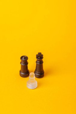 Satranç konsepti: Beyaz piyon sarı arka planda siyah kral ve vezire meydan okuyor, cesaret ve stratejik düşünceyi gösteriyor