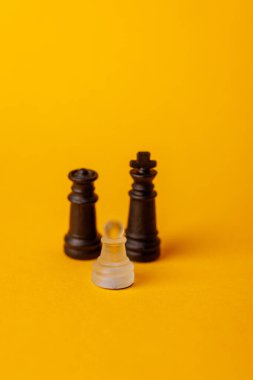 Tek beyaz piyon, rekabeti, gücü ve stratejiyi temsil eden sarı bir yüzeyde siyah kral ve vezirle karşı karşıya gelir.