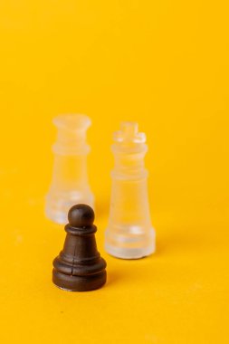 Siyah piyon, sarı yüzeyde satranç oyununda strateji, çatışma ve liderliği temsil eden beyaz kral ve vezirle karşılaşır. Cesur bir güç karşıtlığı