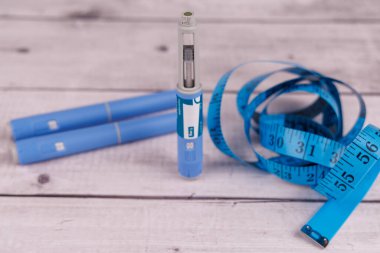 Ozempic (semaglutide) kalemi dikey olarak kalemler ve beyaz bir masanın üzerine bir mezura ile yerleştirilmiştir.