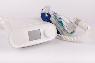 Beyaz arkaplanda uyku apnesi tedavisi için ekranı, hortumu ve maskesi olan beyaz CPAP makinesi