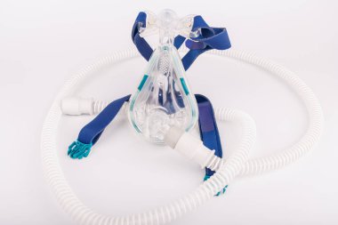 Gece solunum terapisi için tasarlanmış bir tıbbi CPAP ünitesi, beyaz bir arka plana yerleştirilmiş maske, hortum ve ekran içeriyor.
