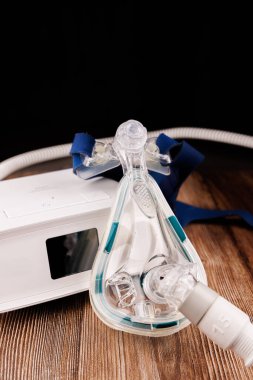 Maskesi ve görüntüsü olan beyaz bir CPAP makinesi, CPAP 'nin uyku apnesi tedavisinde uygulamasını gösteren koyu ahşap bir masada sergileniyor.