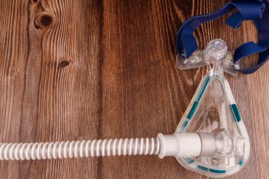 Görüntü, uyku apnesi tedavisinde kullanıldığını vurgulayan, koyu renk ahşap bir masaya yerleştirilmiş beyaz bir CPAP makinesini içeriyor.