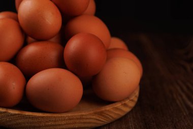 Koyu ahşap bir yüzeyde, tahtadan bir tabakta duran bir dizi taze kahverengi yumurta, gıda fiyatı enflasyonu ve ekonomik etki kavramını gözler önüne seriyor..