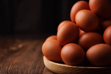 Kahverengi yumurtalarla dolu ahşap bir tabak, artan gıda harcamalarının ekonomik sonuçlarını gösteren koyu bir ahşap yüzeye yerleştirilmiştir..