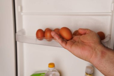 Bir el, yumurta kapmak için buzdolabının içine uzanır ve yumurta fiyatlarındaki artışı ve gıda enflasyonunu görsel olarak temsil eder..