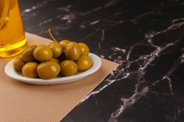 Taze zeytin ve yağ şişesi siyah arkaplanlı, siyah mermer bir masanın üzerinde düzgünce dizilmiş.