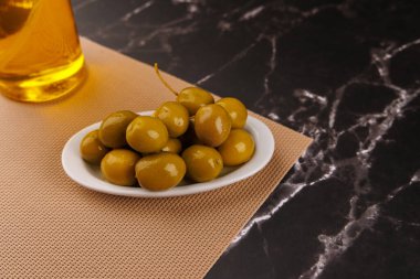 Yeşil zeytinleri bir tabağın üzerinde, siyah mermer üzerinde zeytinyağı şişesinin yanında, zarif koyu arkaplanlı.