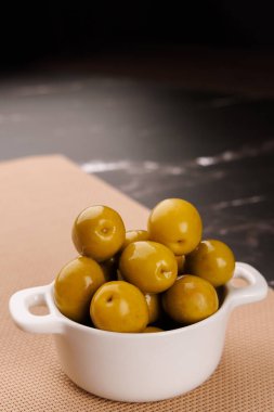 Yeşil zeytinli servis tabağı siyah mermer bir masa üzerinde yumuşak siyah arka plan, yakın görüş