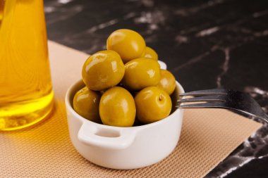 Siyah mermer, siyah arka planda, yağ şişesinin yanındaki tabaktan zeytin alan kürdanlı parmaklar.