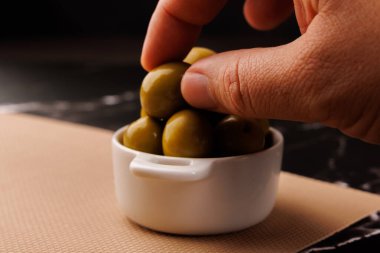 Basit bir kürdan, cam bir yağ şişesinin yanında bir zeytin ve siyah mermer bir yüzey üzerinde servis tabağı yakalar.