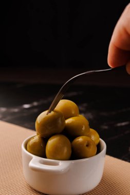 Zeytin ve yağ şişesinin üst görüntüsü, siyah mermer masa üzerinde bir zeytin kaldırıyor, koyu arkaplan