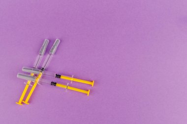Camdan yapılmış heparin dolu şırıngalar tıbbi hassasiyetle menekşe arkaplanına yerleştirilmiş.