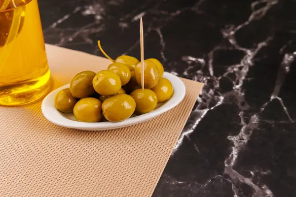 Zeytinler tabakta ve yağ şişesi mermer bir masanın üstünde dramatik siyah bir arka plan, üst manzara