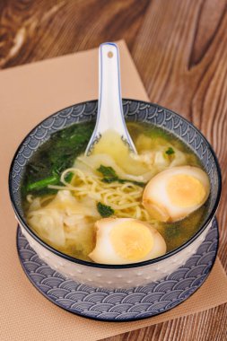 Beyaz bir kasede ramen ve haşlanmış yumurta. Kırsal kesimde mavi bir kaşıkla servis ediliyor..