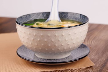 Lezzetli ramen, yumurta, wonton ve ahşap zemin üzerinde seramik kaşıkla servis edilir..