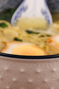 Lezzetli bir kase erişte, wonton ve yumurta, ahşap arka planda seramik kaşıkla eşleştirilmiş..