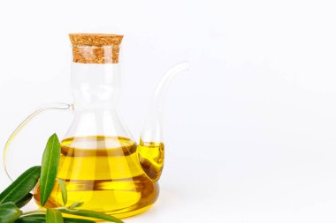 Yağ şişesi ve pürüzsüz beyaz bir yüzey üzerinde taze zeytin dalı ile gösterilen kırsal zerafet..