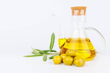 Akdeniz sahnesinde beyaz zeytin yağı şişesi, taze zeytin ve zeytin filizi var.