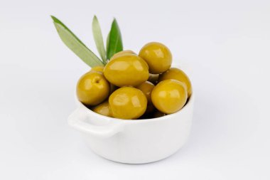 Zeytin dallı beyaz bir kasede taze yeşil zeytin, temiz beyaz arka planda minimum kompozisyon.